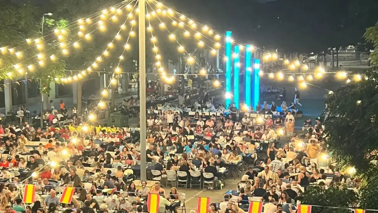 Multitudinaria cena al aire libre en las fiestas Cuarte de Huerva, iluminada por guirnaldas de luces y con gente disfrutando de la noche.