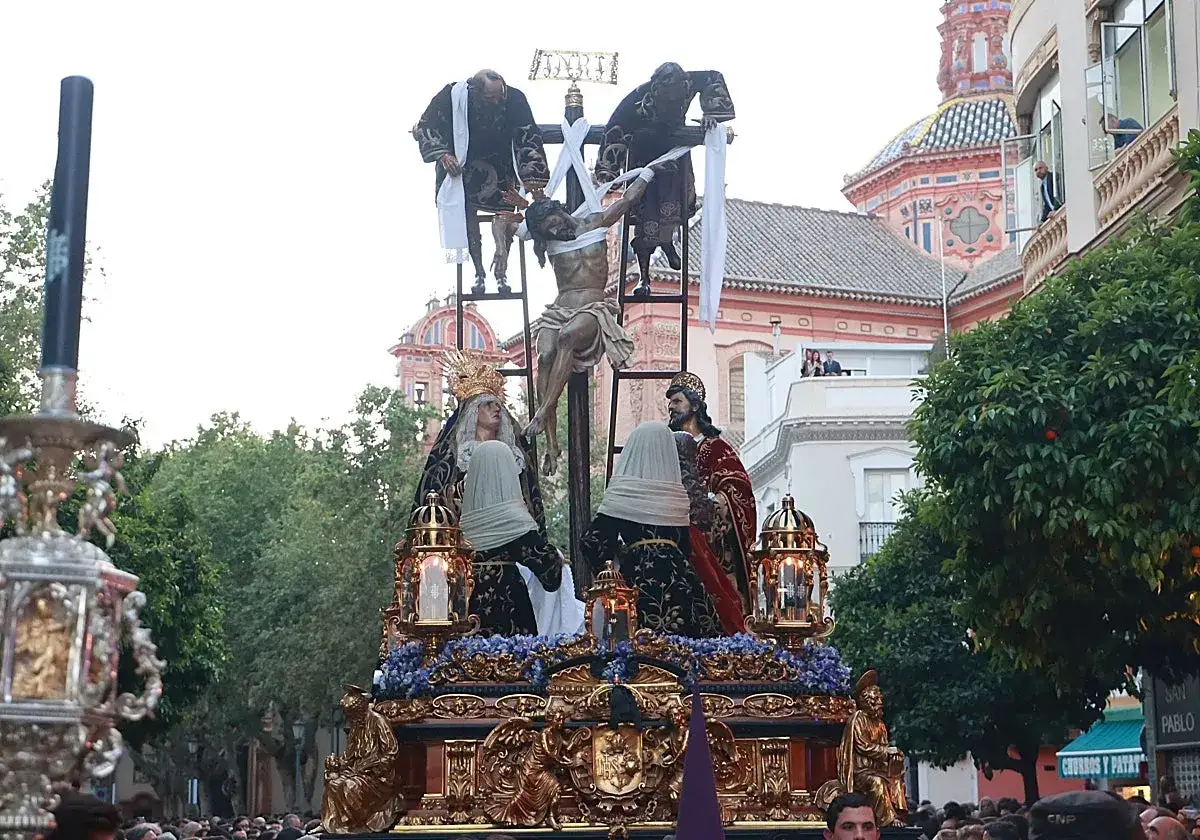 Procesiones Semana Santa Jueves Santo: paso con Cristo crucificado, la Virgen y San Juan, adornado con flores y faroles, desfila entre la multitud.