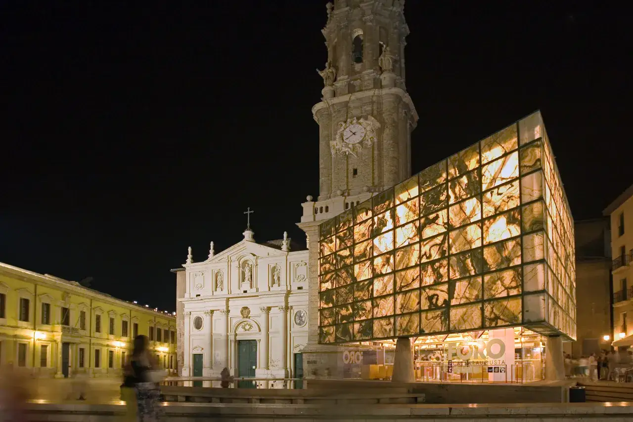 Edificio moderno con fachada iluminada junto a la Basílica del Pilar, parte de la ruta Caesaraugusta.