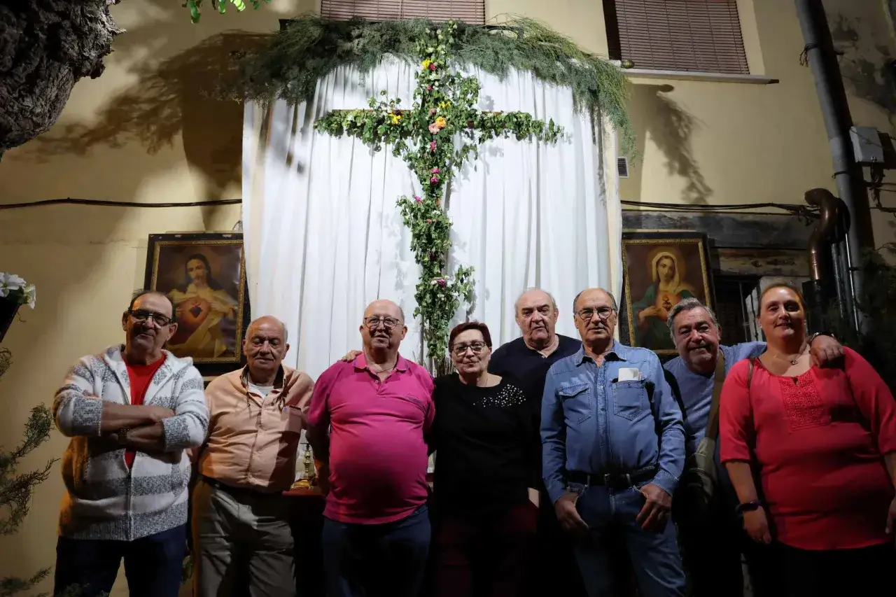 Un grupo de personas posa frente a una cruz decorada con flores y follaje, quizás celebrando los mayses.