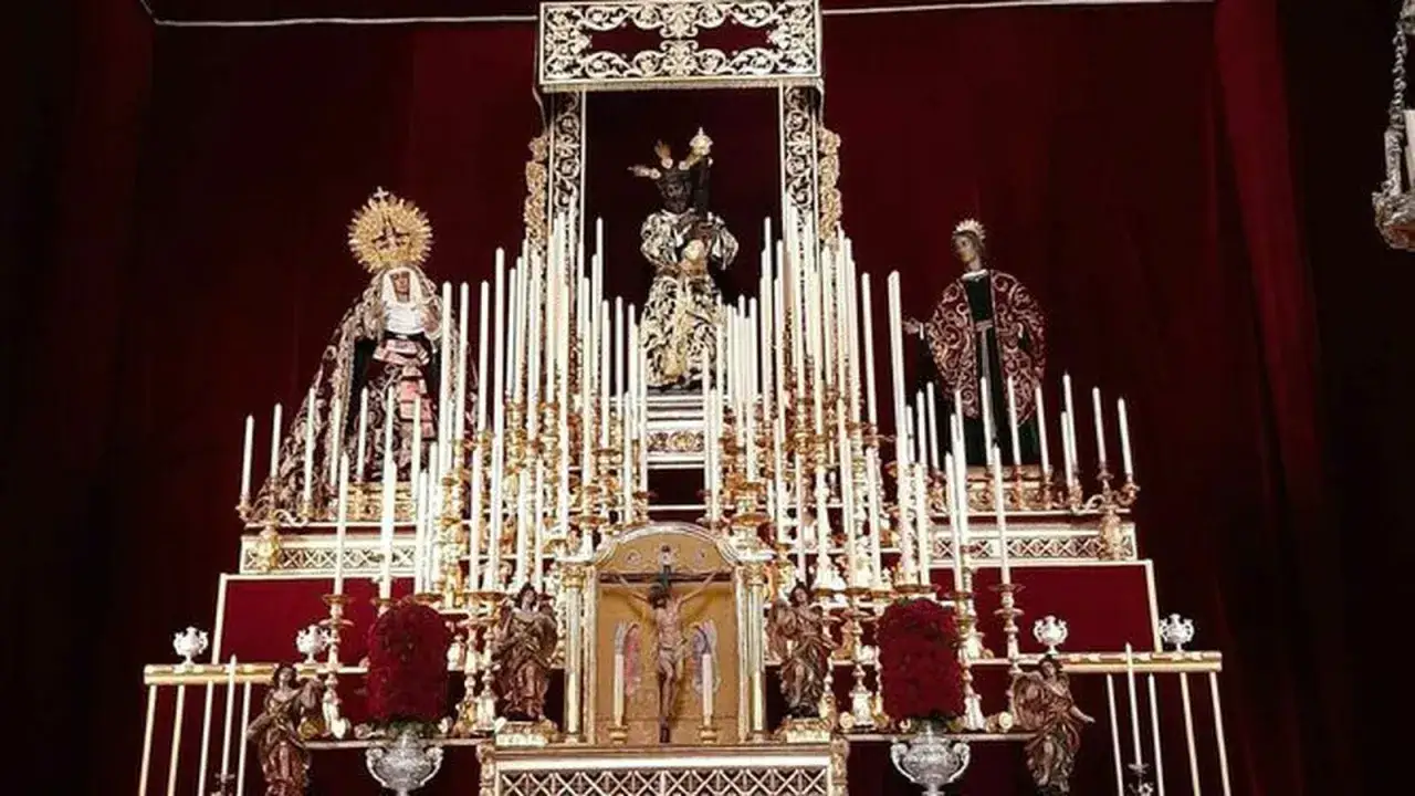 Escenario religioso con figuras y velas. Se aprecia un Cristo crucificado, una virgen y un santo, parte de lo que es un quinario.