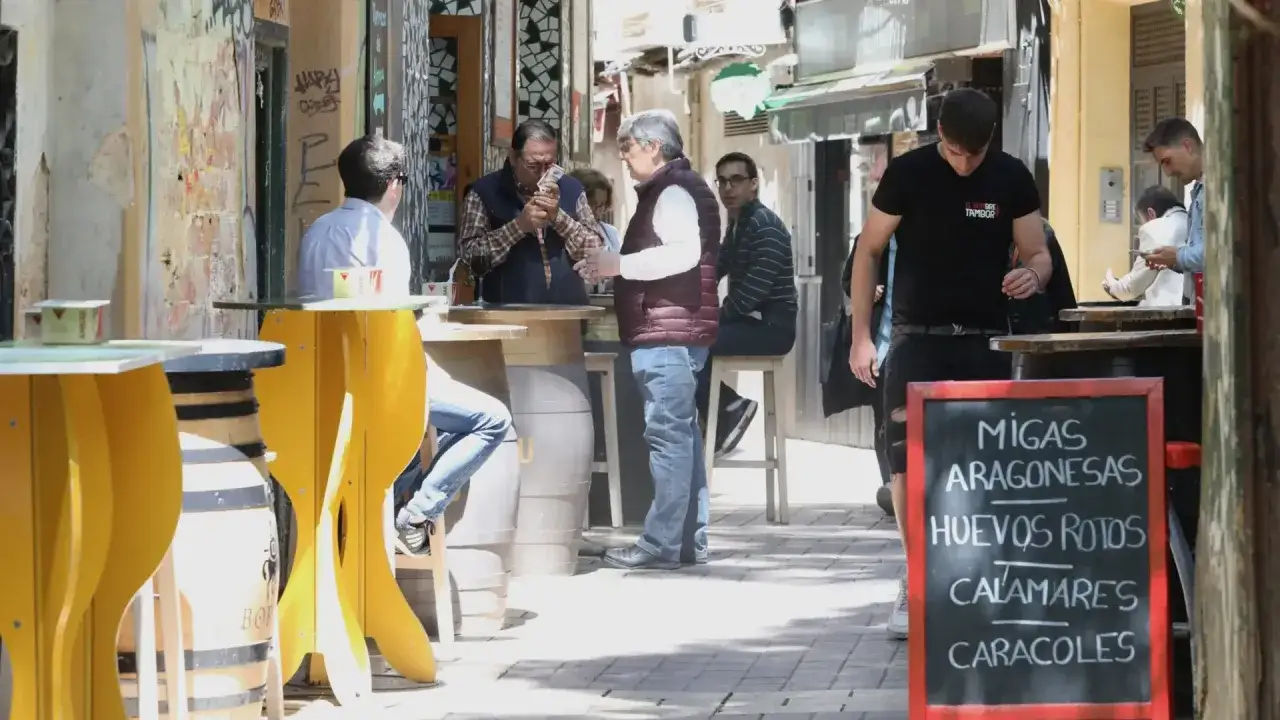 Gente disfrutando de tapas en Zaragoza. Un cartel anuncia migas aragonesas, huevos rotos, calamares y caracoles.