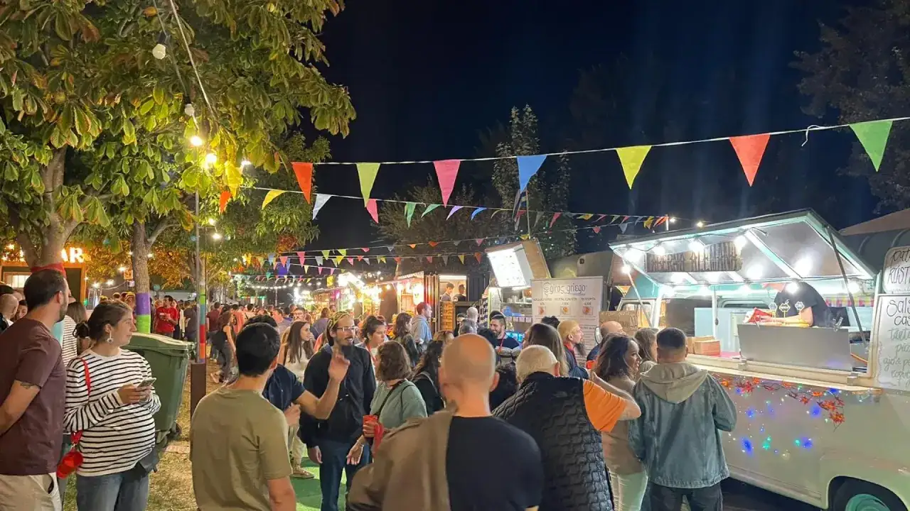 Noche de fiesta con food trucks Zaragoza Pilares. Gente disfrutando de la comida callejera bajo luces y banderines de colores.