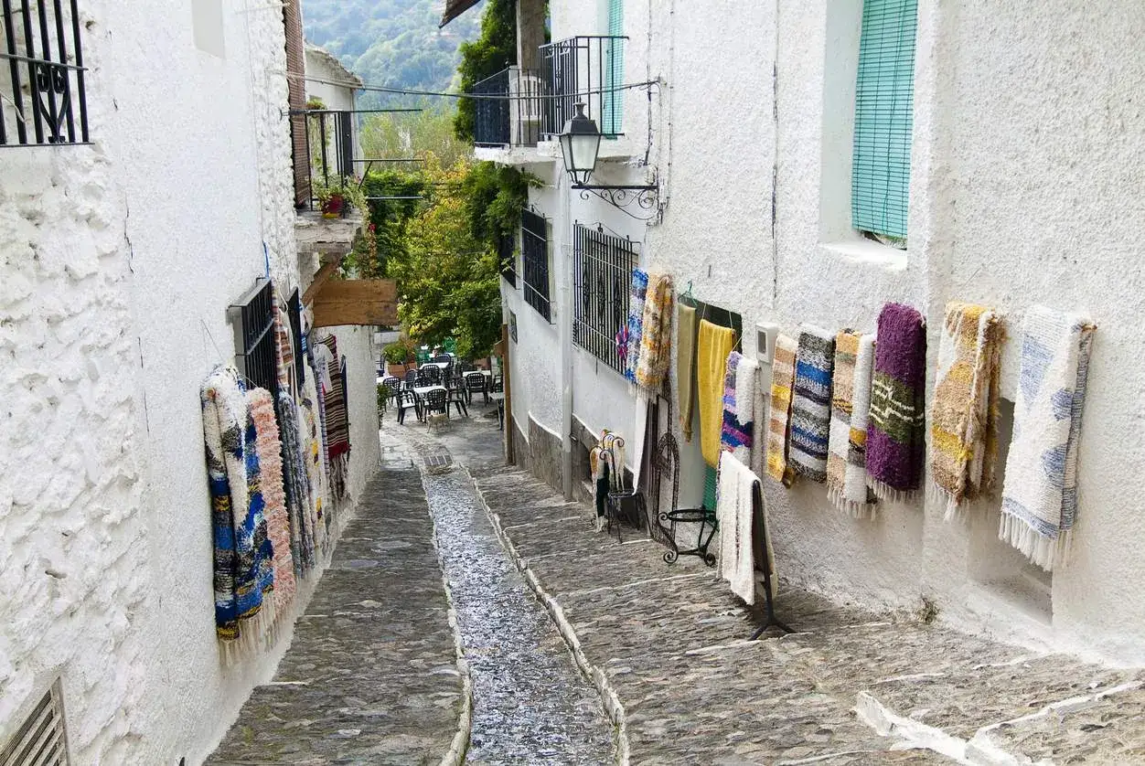 Calle empedrada con alfombras colgadas, ideal para ver cerca de Granada.