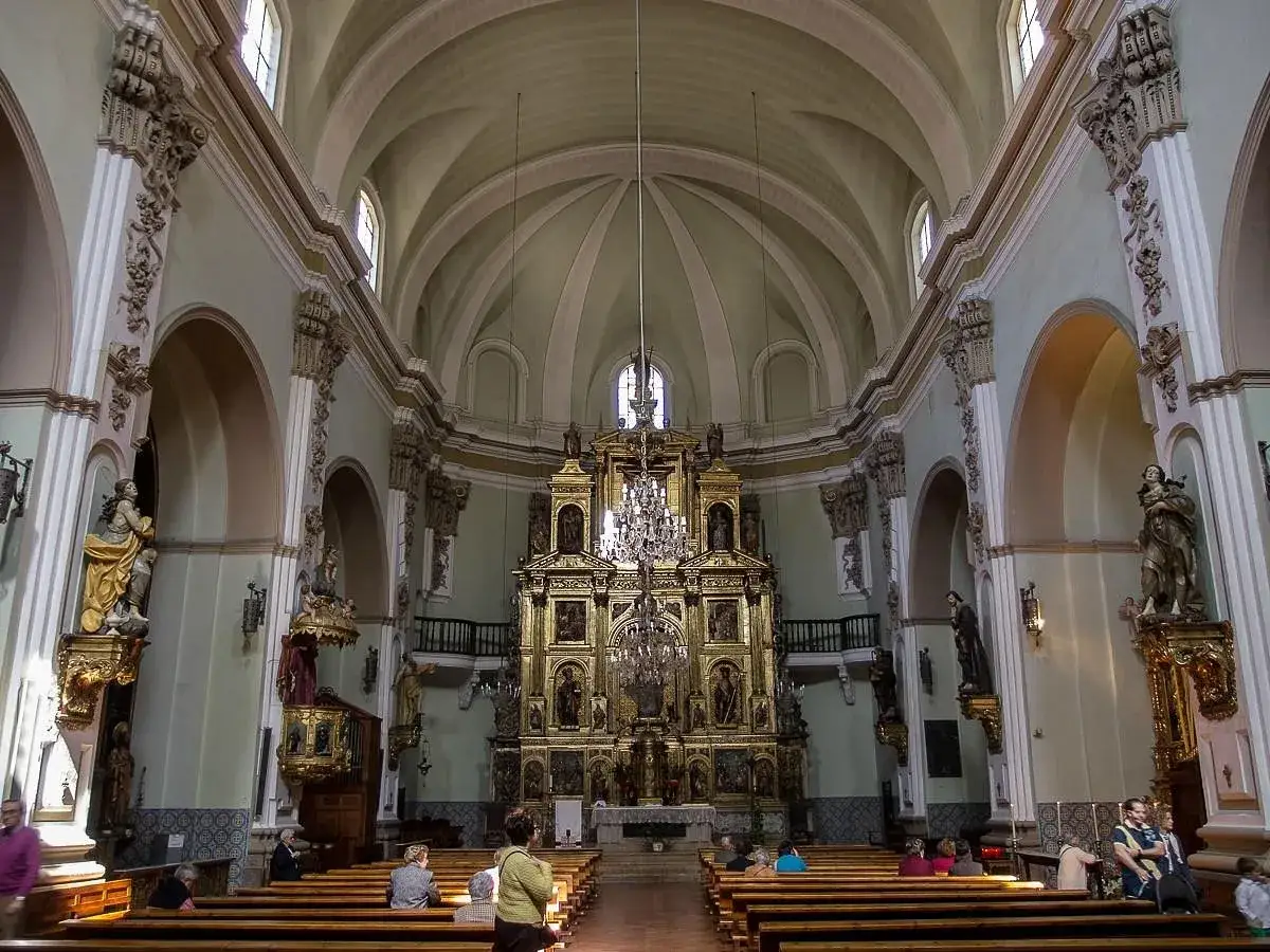 Interior de la iglesia de San Gil Abad en Zaragoza, con un retablo dorado y bancos de madera.