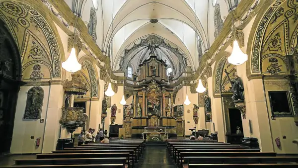 Interior de la iglesia de la Magdalena en Zaragoza, con bancos de madera, un retablo dorado y esculturas.