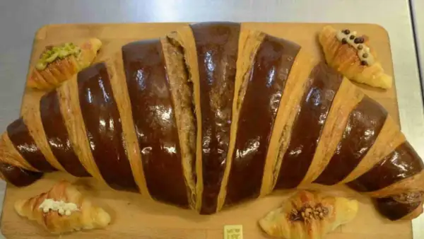 Un croissant gigante con glaseado de chocolate y pequeños croissants decorados, perfectos para un desayuno en Zaragoza.