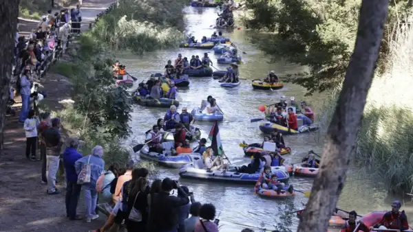 Gente en balsas y kayaks disfrutan de la bajada del canal, rodeados de espectadores en la orilla.
