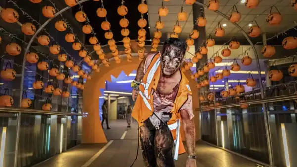 Un espeluznante zombie con maquillaje de Halloween avanza bajo un arco decorado con calabazas en Puerto Venecia.
