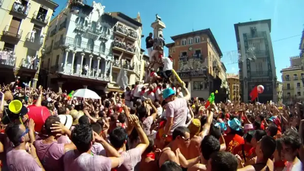 Multitud celebra cuando son vaquillas en Teruel. Gente en una plaza con edificios históricos, algunos subidos a un monumento.