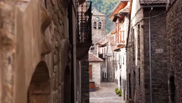 Calle empedrada en un pueblo de Aragón, con casas de piedra y un campanario al fondo.