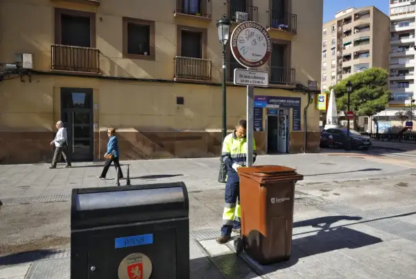 Un trabajador recoge un contenedor marrón en Zaragoza, bajo un sol radiante, como parte de la fiesta del sol.