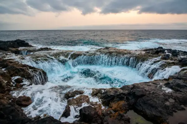 El mar choca contra las rocas volcánicas, creando una cascada de agua azul en un agujero natural. Un lugar impresionante que ver en Gran Canaria.
