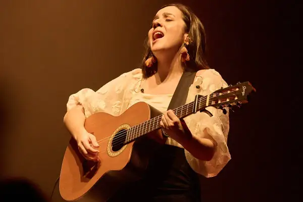 Valeria Castro Zaragoza canta con pasión, guitarra en mano, bajo una luz cálida.