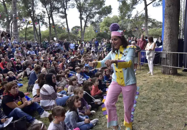 Actriz con traje colorido anima a niños en un espectáculo de marionetas en el parque.