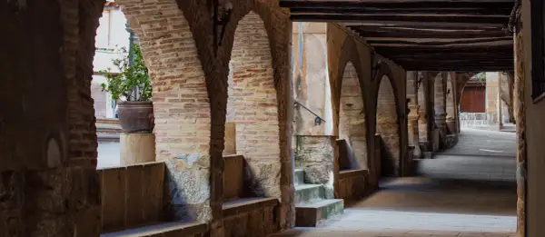 Pasaje abovedado de piedra y ladrillo con arcos, bancos de piedra y una planta en maceta. Un lugar con encanto para pasear y descubrir la fresneda que ver.