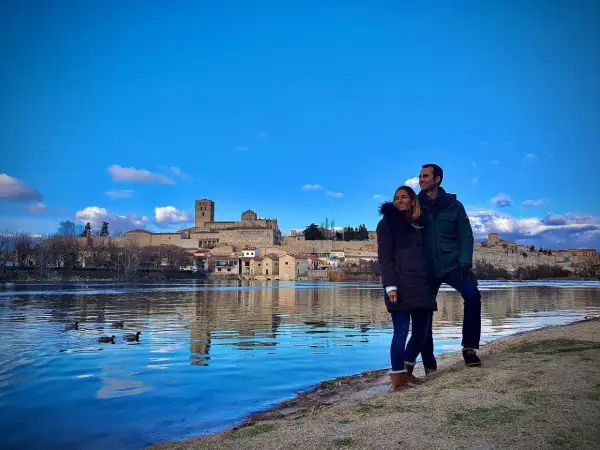 Pareja disfruta de la vista del río Duero y la ciudad de Zamora, un lugar que merece la pena visitar. Patos nadan en el agua azul.