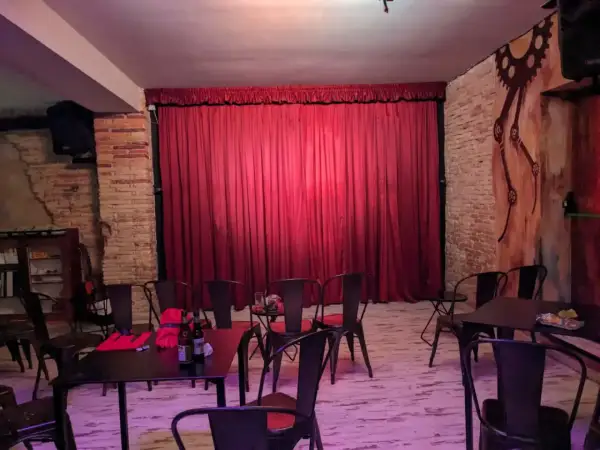 El escenario de el.sotano magico, con cortinas rojas y sillas metálicas, listo para un espectáculo.
