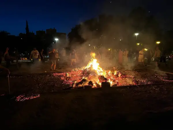 Gente reunida alrededor de una gran hoguera en Zaragoza, celebrando las hogueras de San Juan.