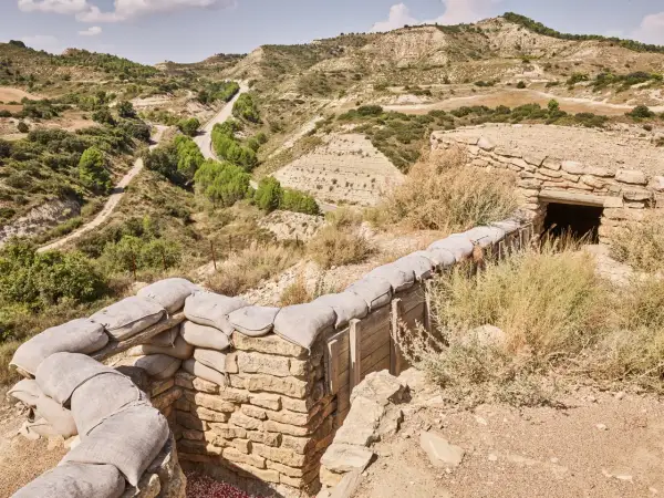Trincheras de la ruta Orwell, con sacos de arena y un refugio de piedra en un paisaje árido y montañoso.