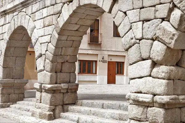 Arcos de piedra del Acueducto de Segovia, un lugar imprescindible que ver en Segovia. Al fondo, la fachada de un edificio con el letrero "El Silencio".