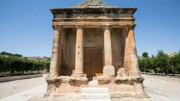 El mausoleo de Fabara, con sus columnas y puerta de madera, se alza imponente bajo un cielo azul.