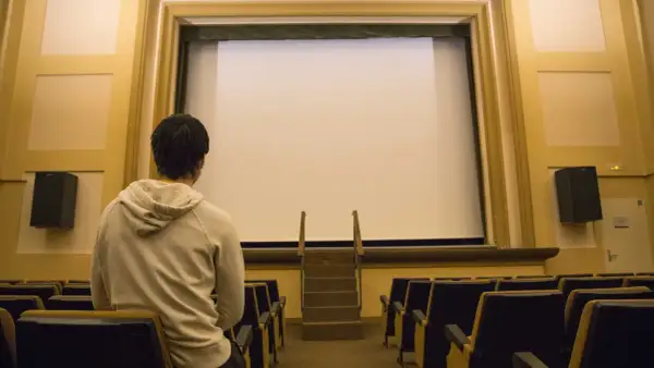 Un joven espera en un cine vacío, listo para disfrutar de una película.
